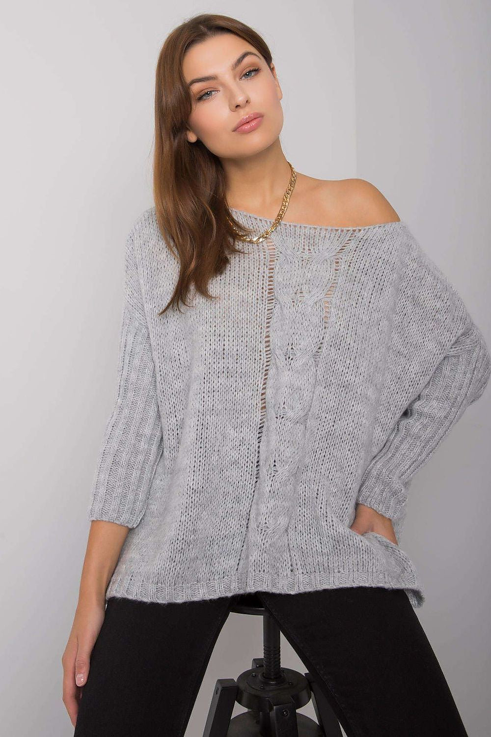 Woman wearing a gray off-shoulder sweater against a plain background