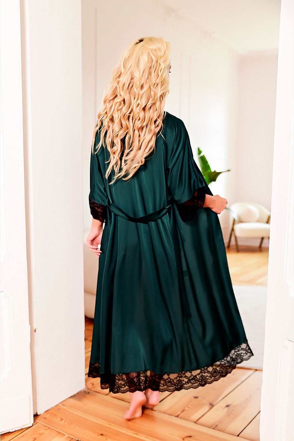 Person wearing a dark green satin robe with lace trim in a room.