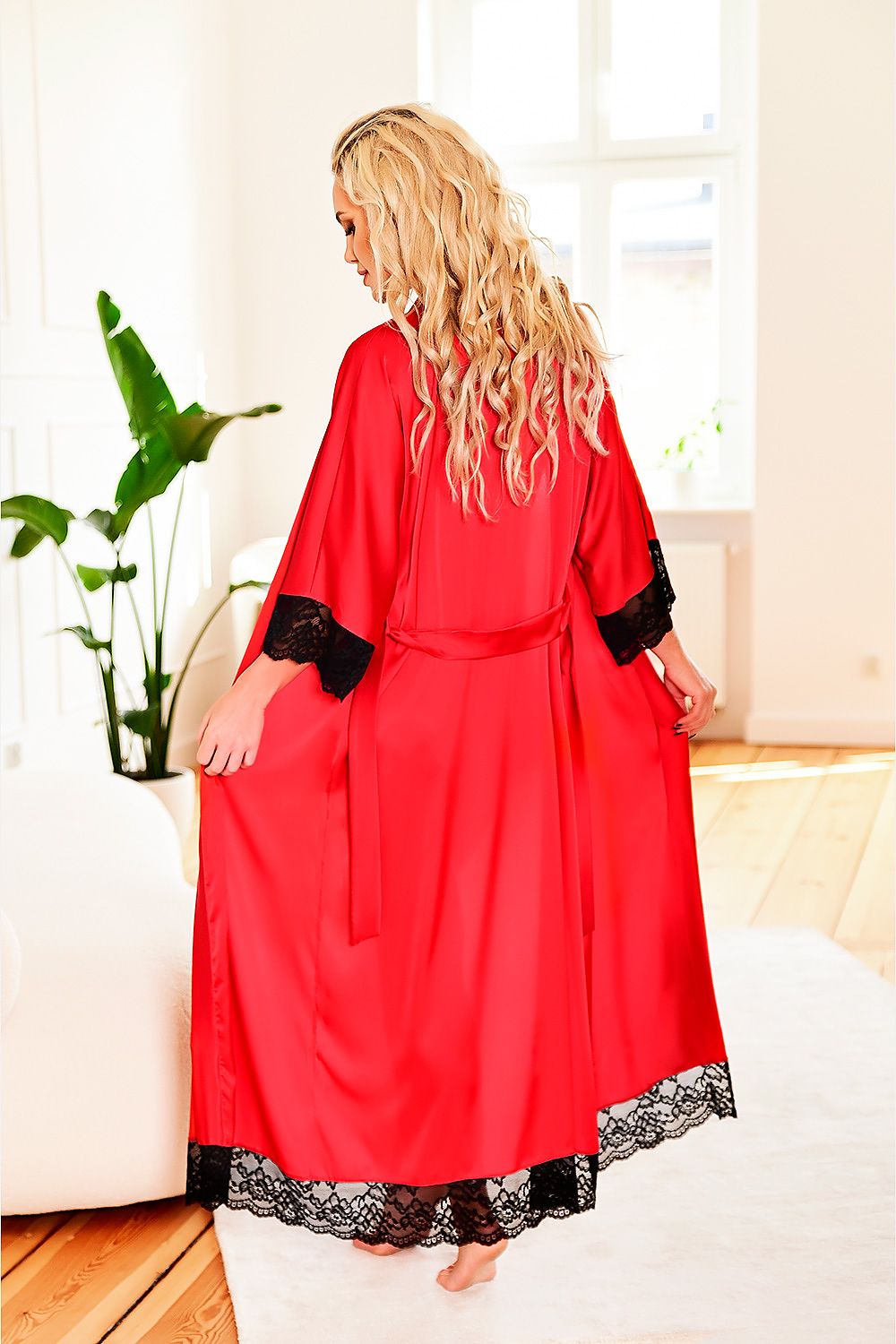 Woman wearing a red satin robe with black lace trim in a bright room.